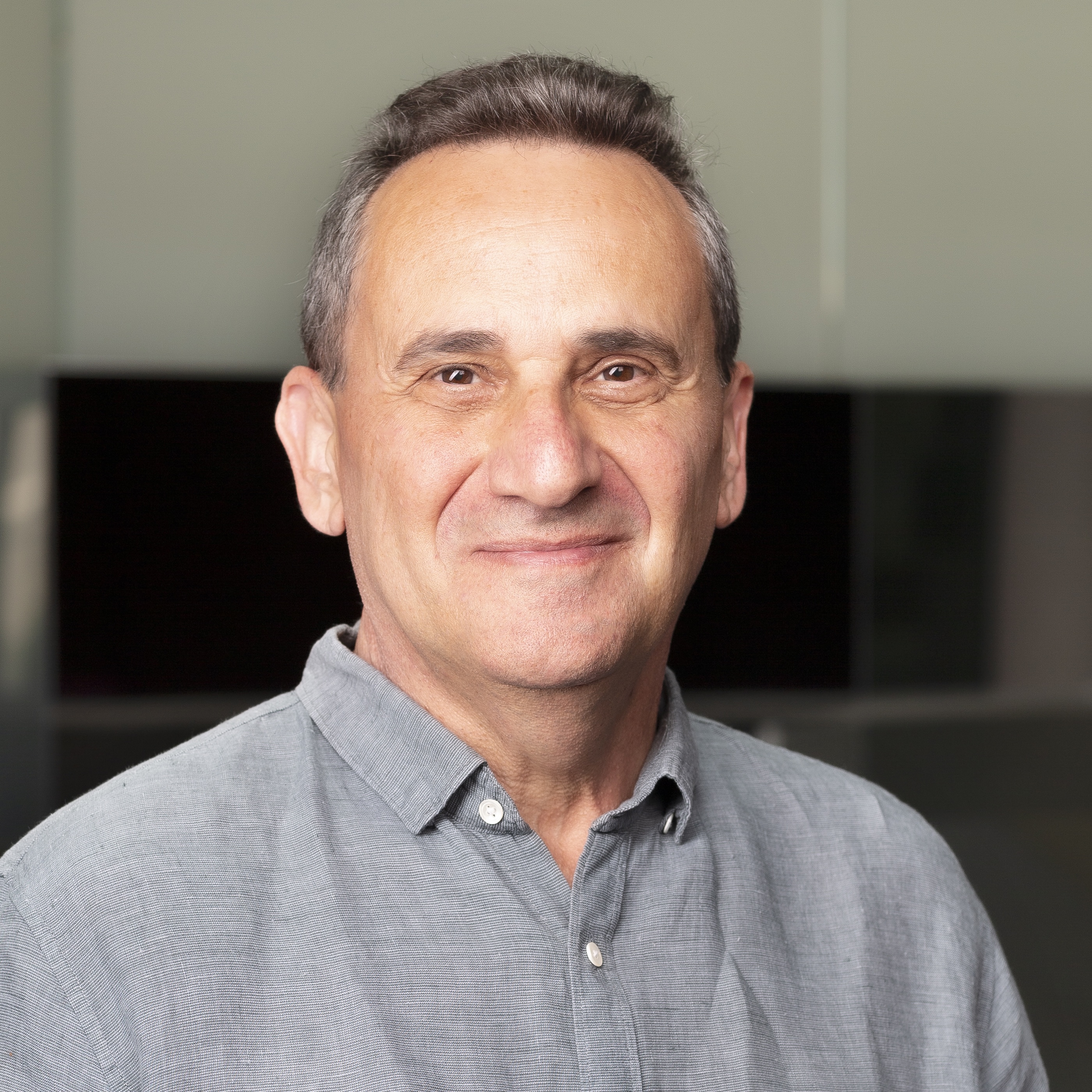 Portrait of a smiling man in a light gray collared shirt against an indoor background